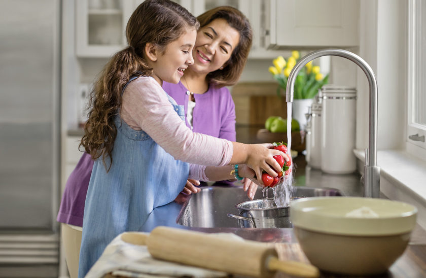 A mother and her daughter washing fresh strawberries in the sink